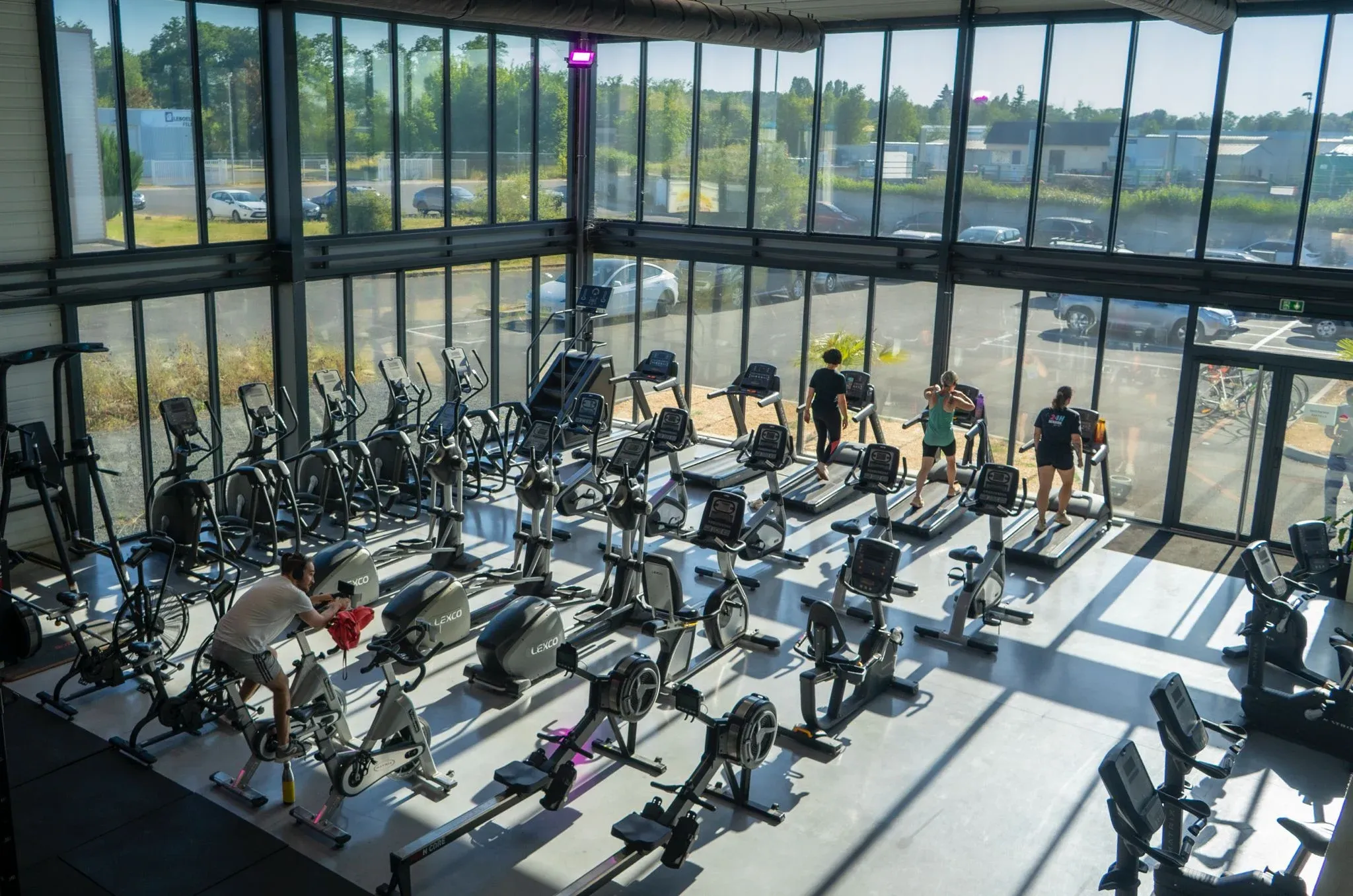 Zone cardio lumineuse de Session Sport avec vélos, rameurs et tapis face aux grandes baies vitrées.