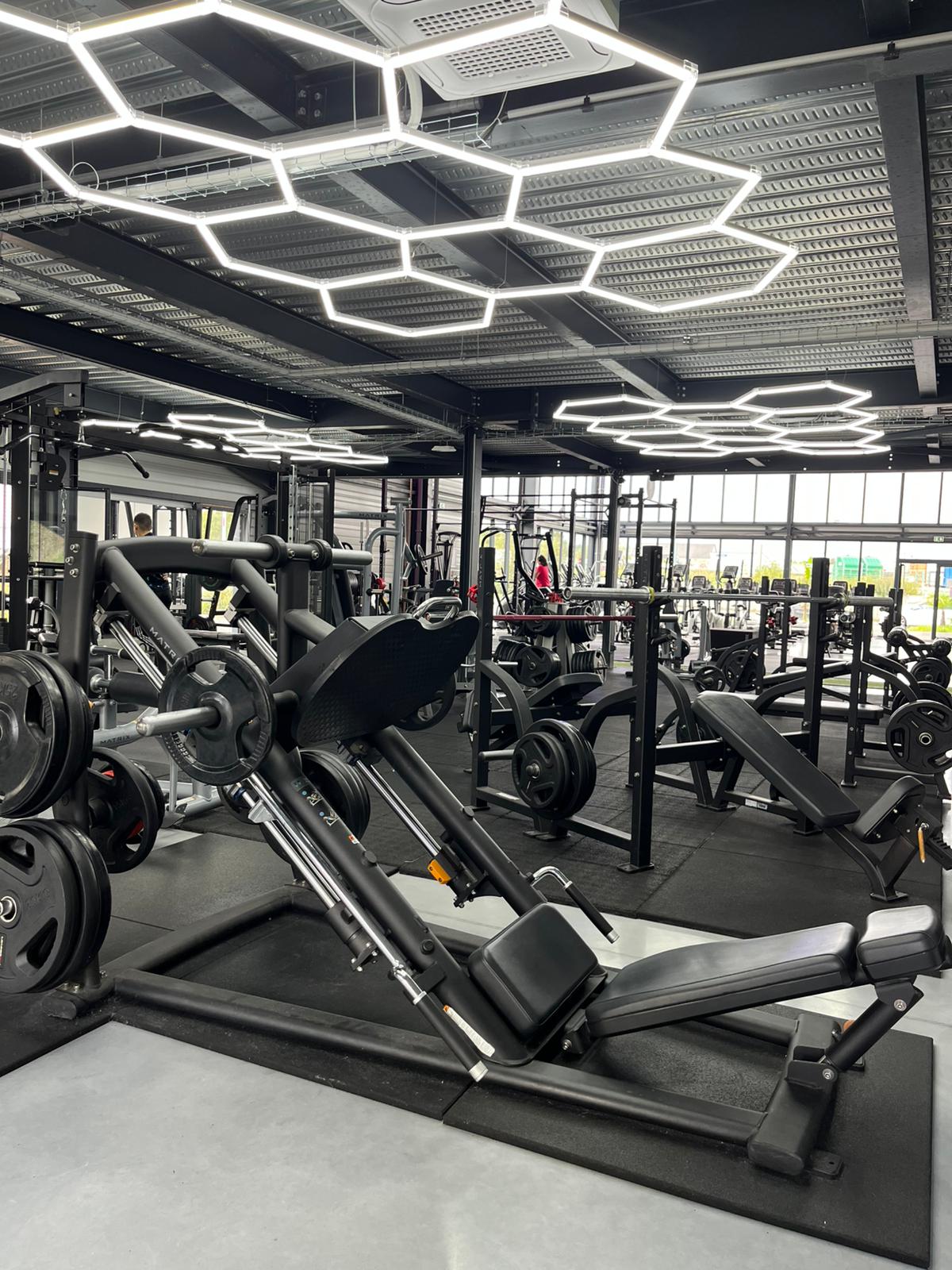 Plateau de musculation Session Sport avec machines guidées, bancs et éclairage hexagonal.